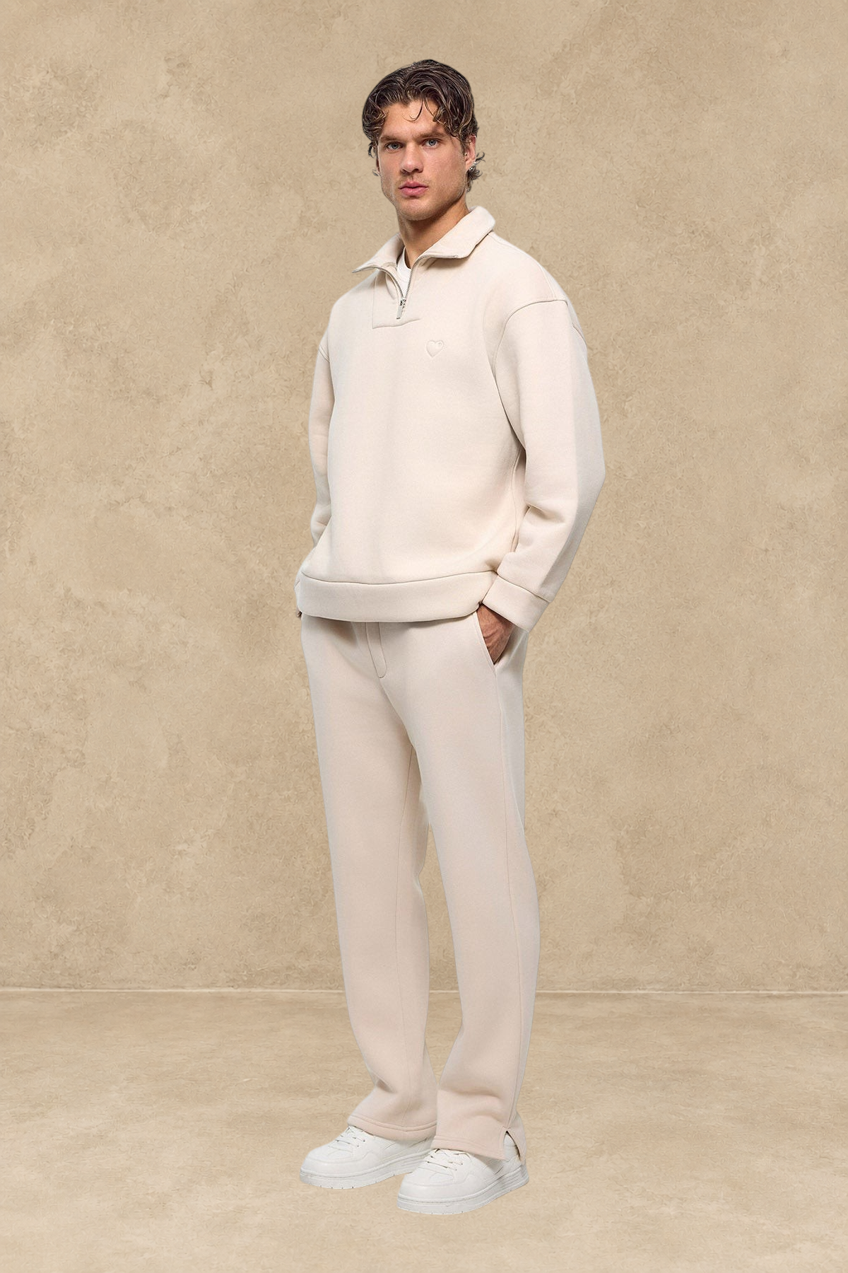 Homme portant un ensemble Stayin beige avec un pantalon jogg à fente à la cheville et un sweat à col zippé