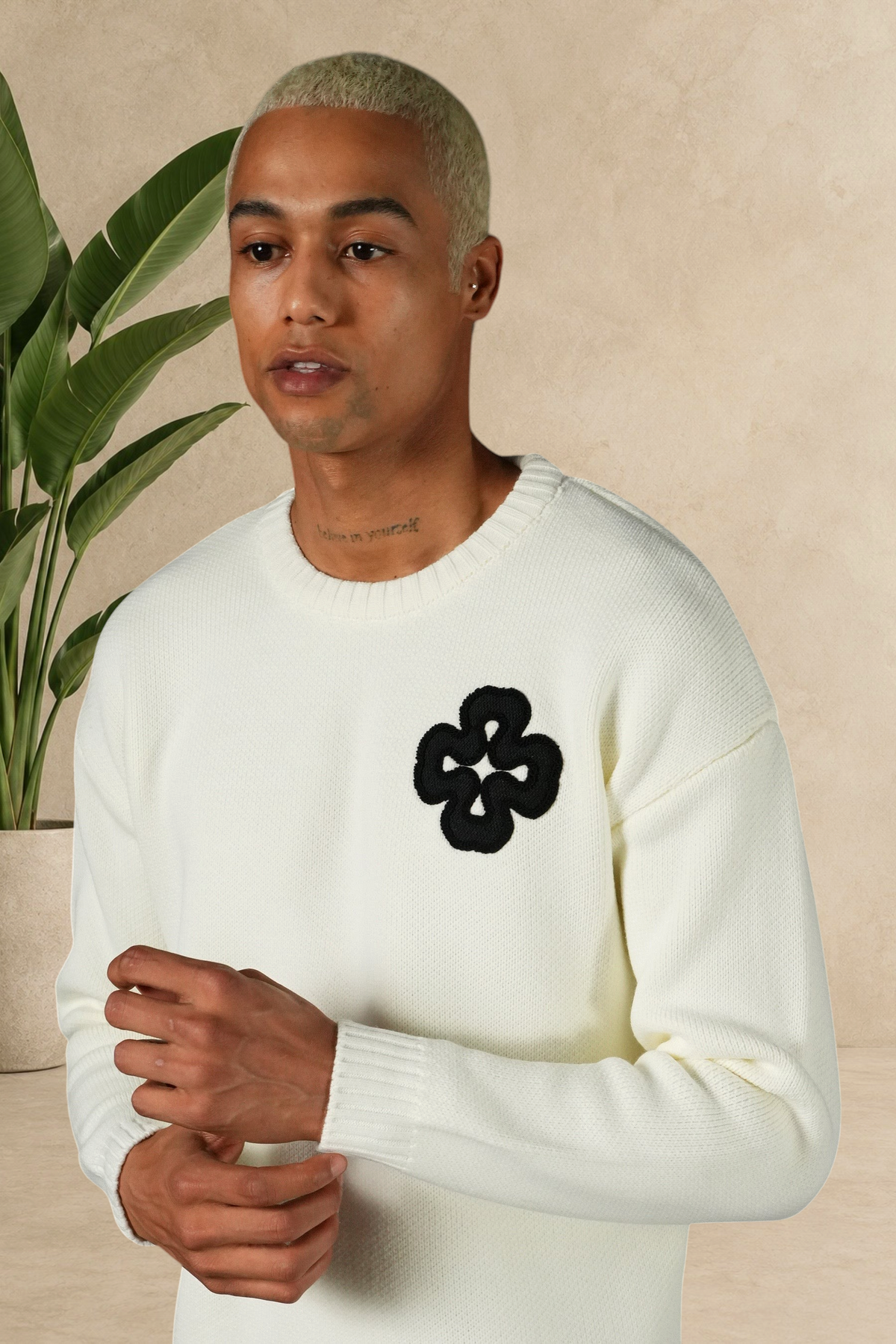 Mannequin portant un pull Stayin blanc en maille épaisse avec un motif trèfle noir brodé sur la poitrine