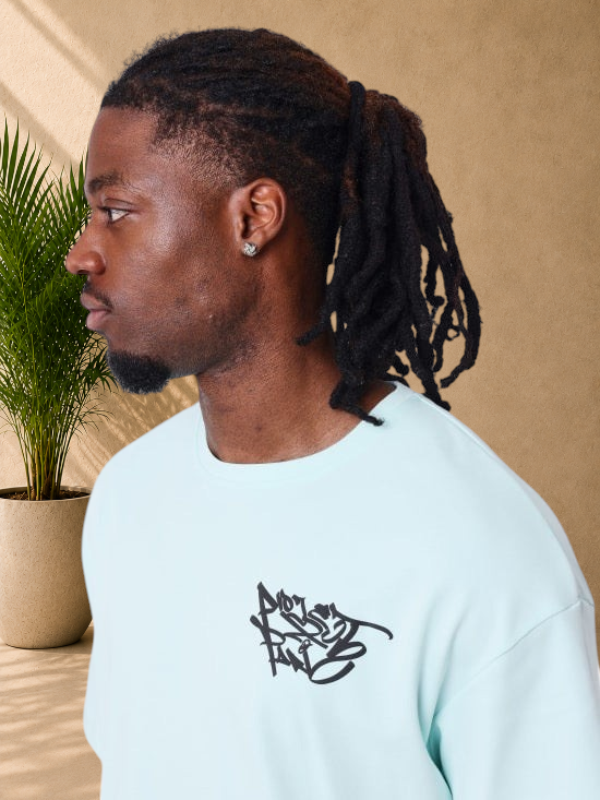 Stayin PXP light green oversized cotton t-shirt with black graffiti logo on chest, worn by a man in profile view.