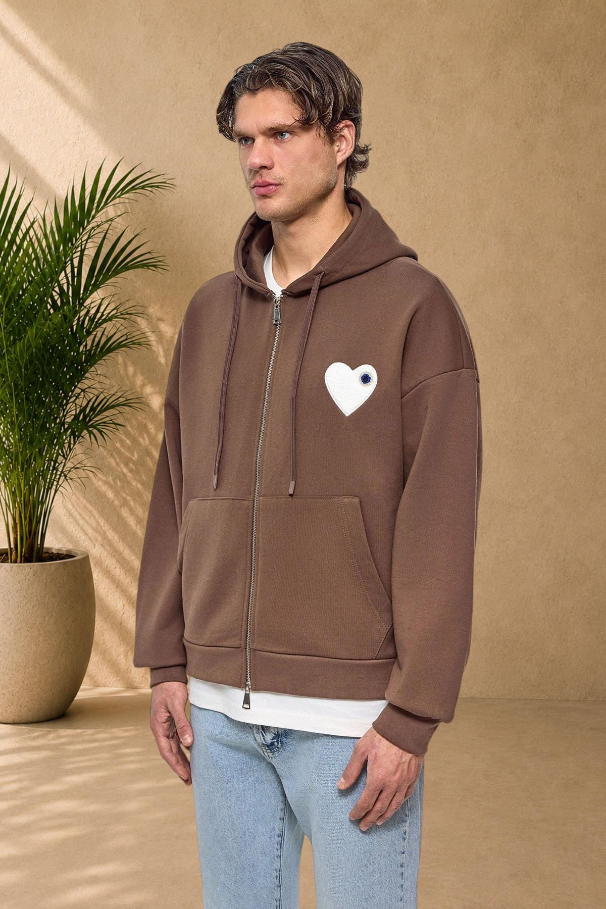 Stayin brown zip-up hoodie with a white heart patch on the chest worn by a male model