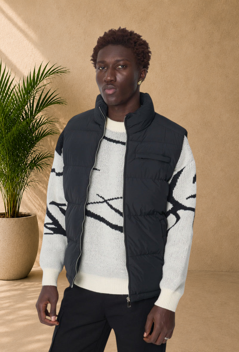 Stayin black sleeveless puffer vest with a high collar and front zipper worn over a patterned knit sweater