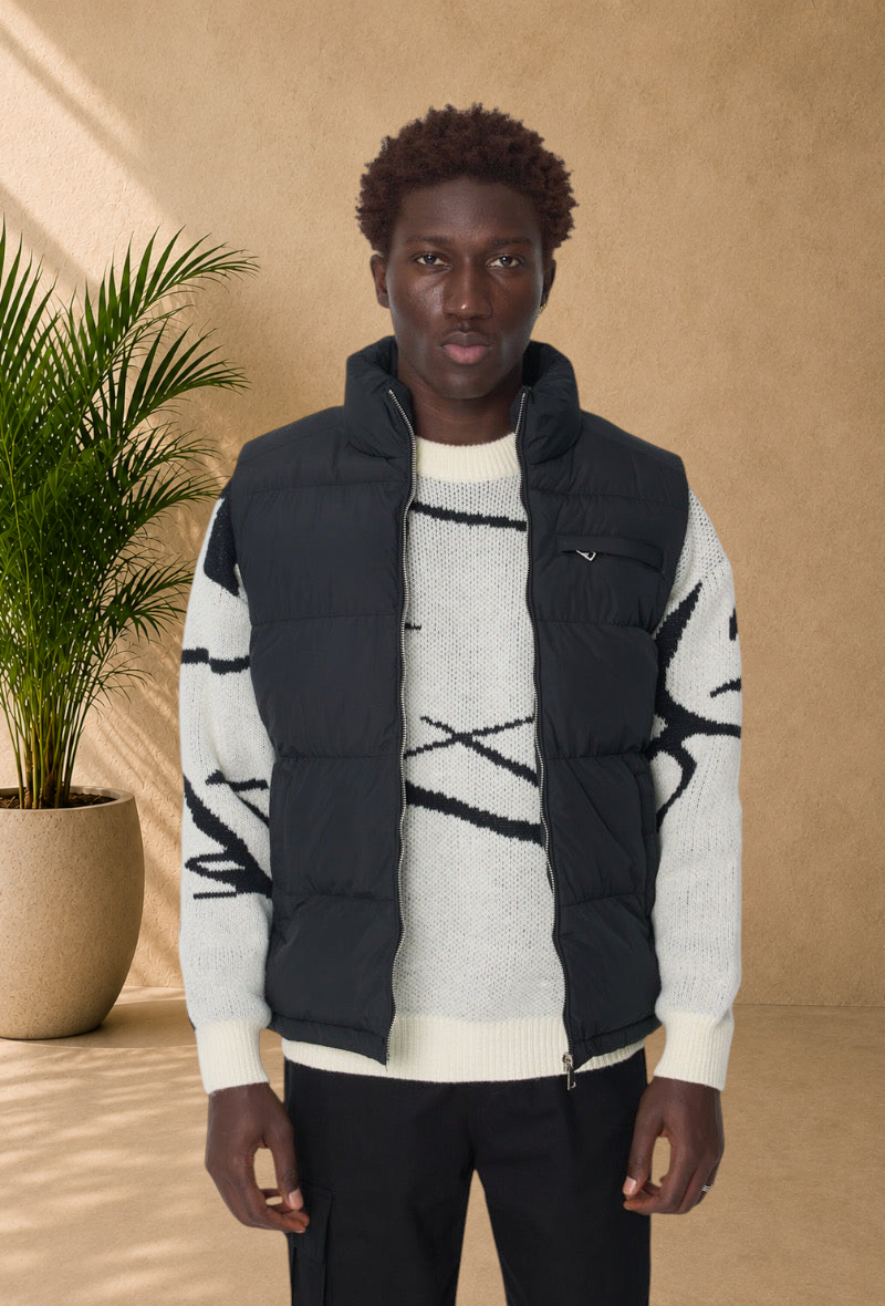 Stayin black sleeveless puffer vest with high collar and front zipper worn by a man over a patterned knit sweater