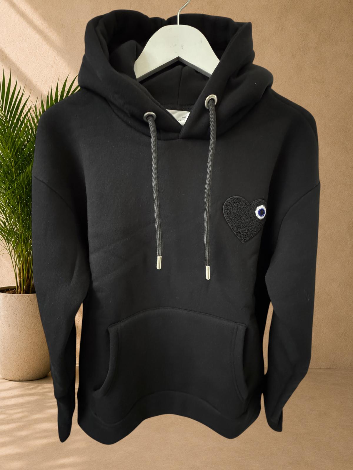 Stayin black quilted hoodie with a small black heart patch and eye detail on the chest, featuring a drawstring hood.