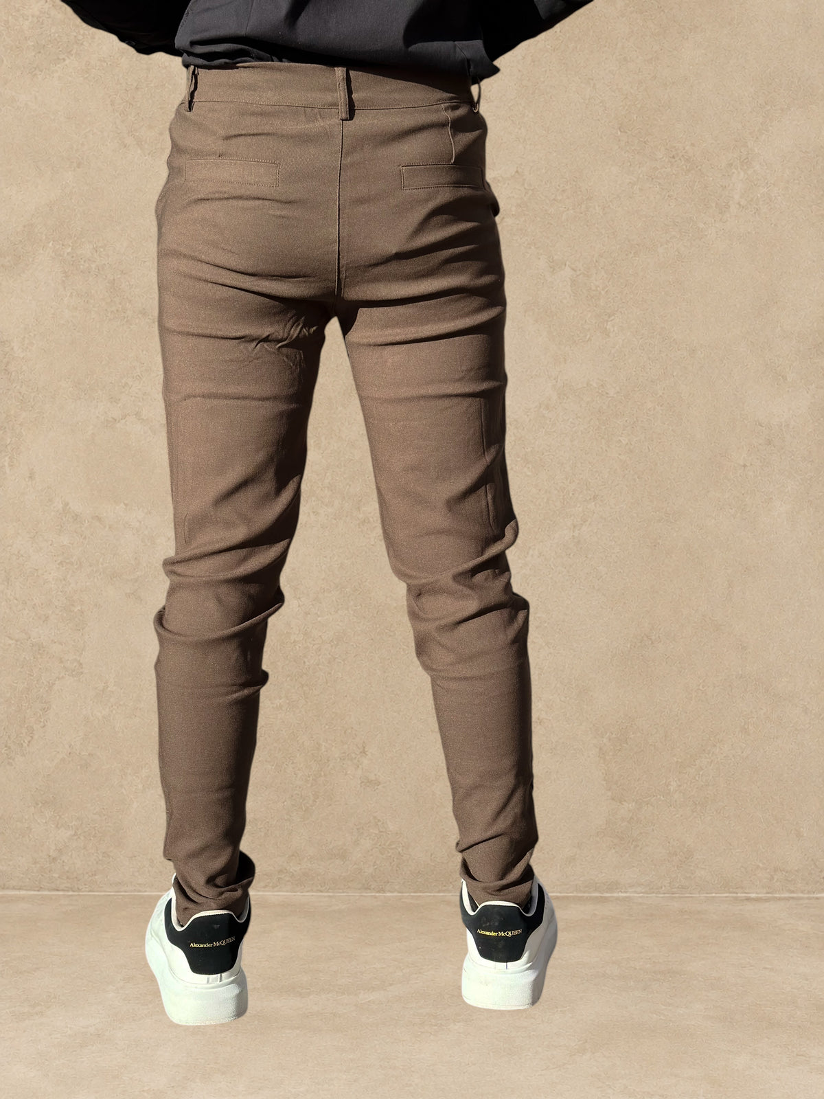 Pantalon Stayin marron coupe cintrée à pinces porté par un homme vu de dos en extérieur